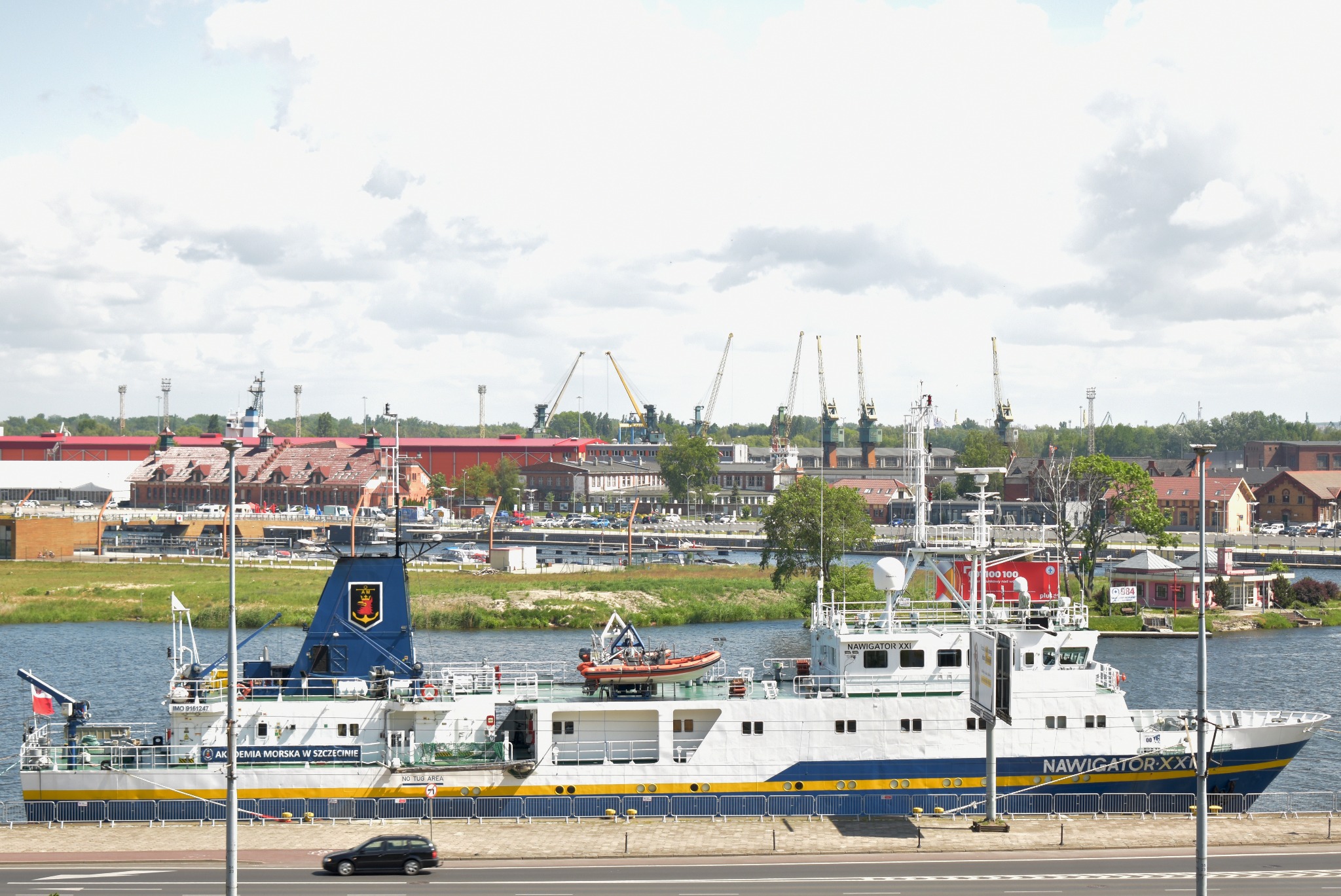 Akademicki statek badawczy Navigator XXI zacumowany w porcie, na burcie napis 'Akademia Morska w Szczecinie', w tle budynki portowe i dźwigi.