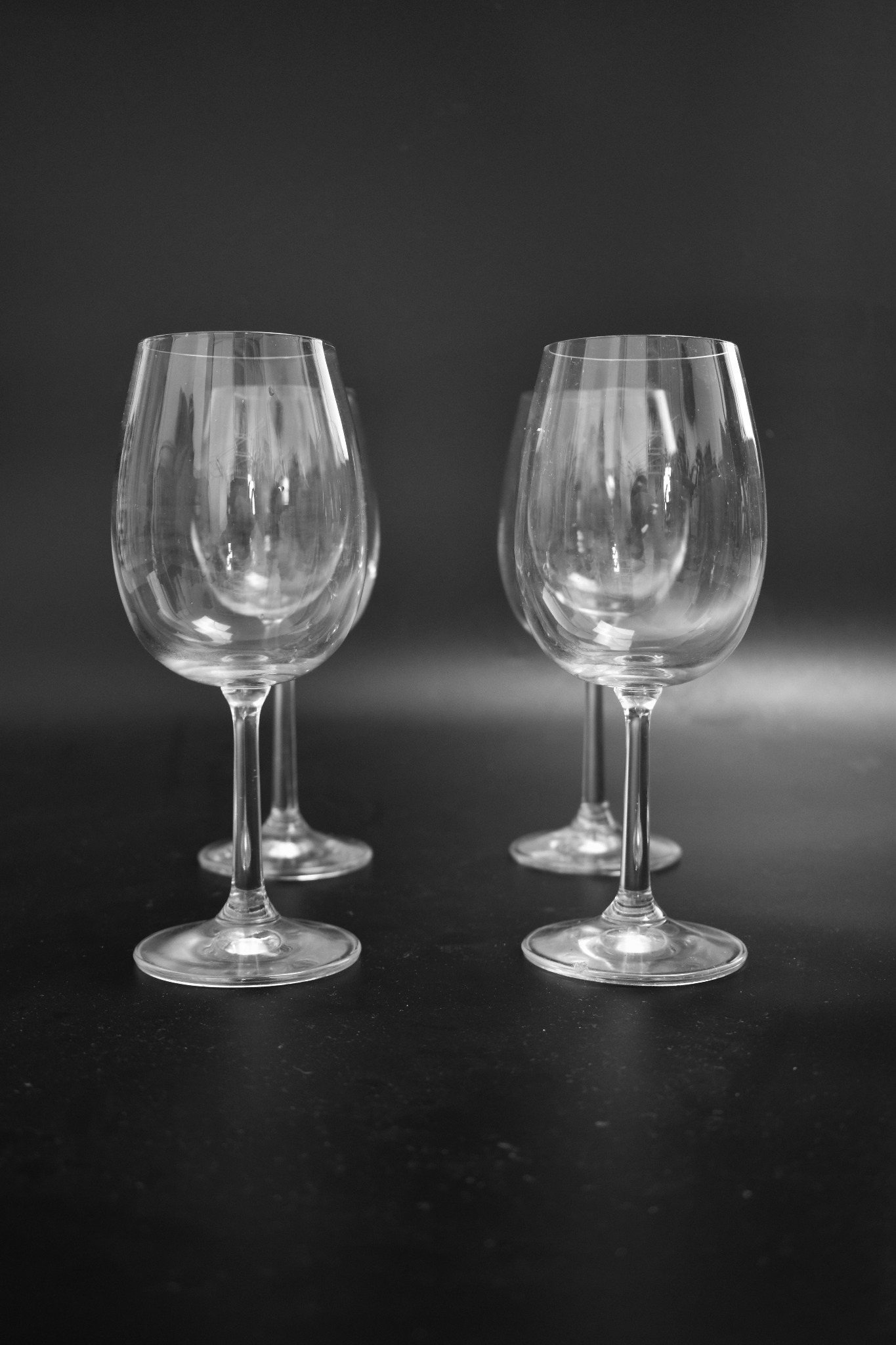 Cztery puste kieliszki do wina ustawione w dwóch rzędach na czarnym tle, z delikatnymi refleksami światła na szkle.