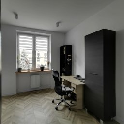 Najmart Sp. z o.o. - Nowoczesny pokój z biurkiem, krzesłem i szafą w ciemnym kolorze. Parkiet ułożony w jodełkę. Na parapecie rośliny doniczkowe. Minimalistyczne oświetlenie sufitowe.