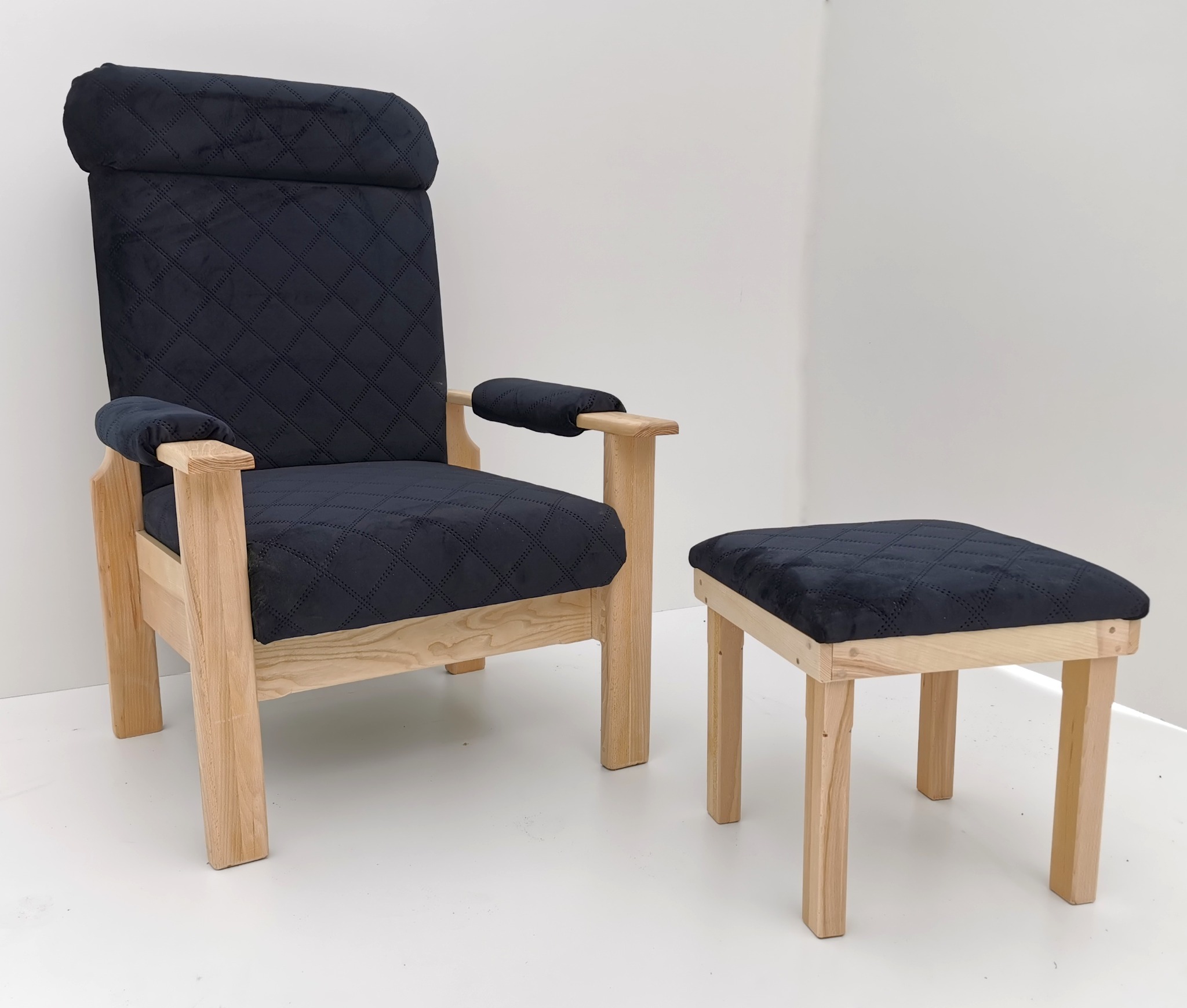 Tapicerowany fotel z podnóżkiem na drewnianej ramie, obity czarnym materiałem w romby, na białym tle. Widok z przodu, jasne drewno, minimalistyczny design.