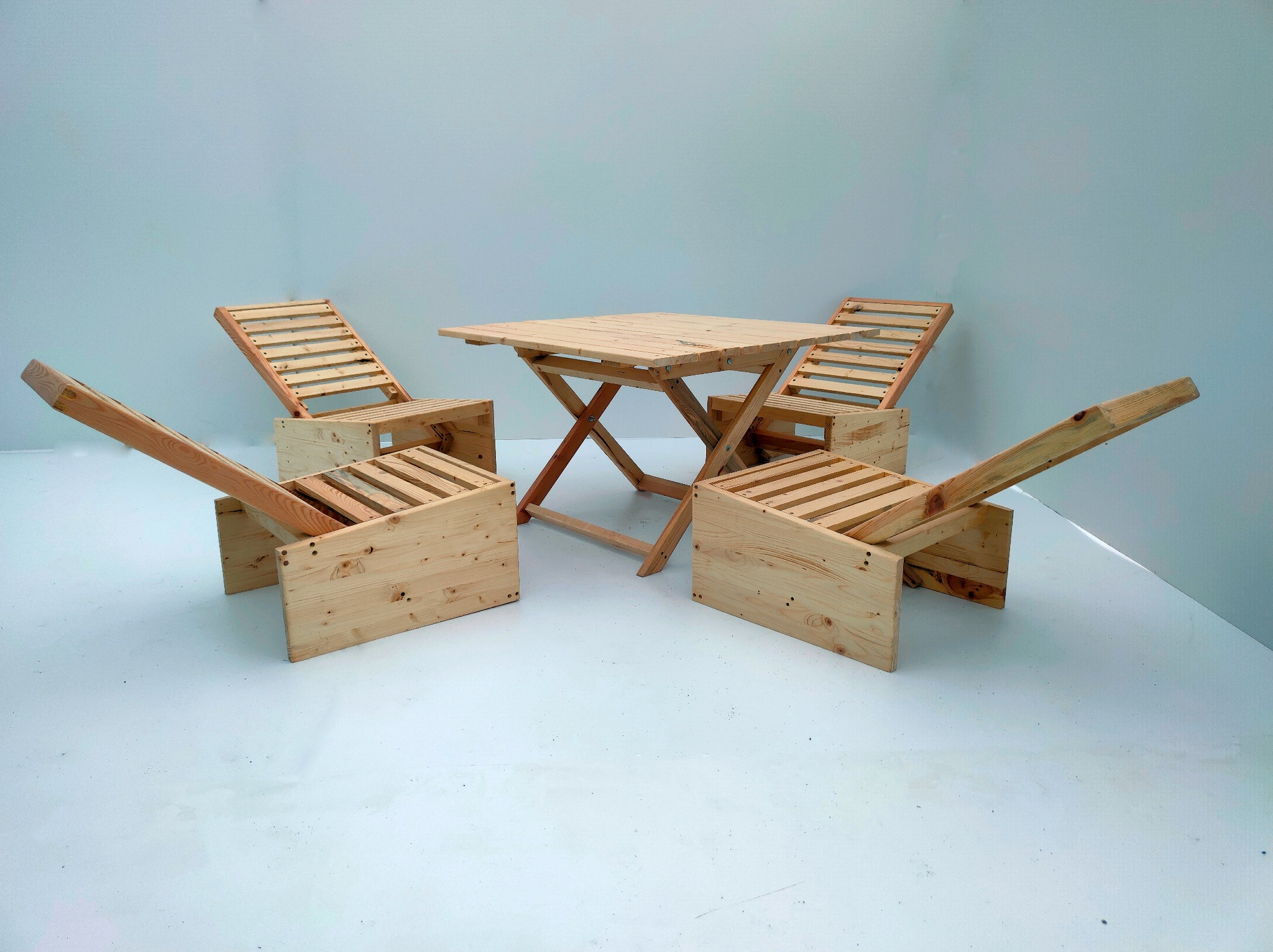 Komplet mebli ogrodowych z jasnego drewna: składany stół i cztery krzesła z oparciami, ustawione na białym tle. Widoczne detale konstrukcyjne i naturalny odcień drewna.