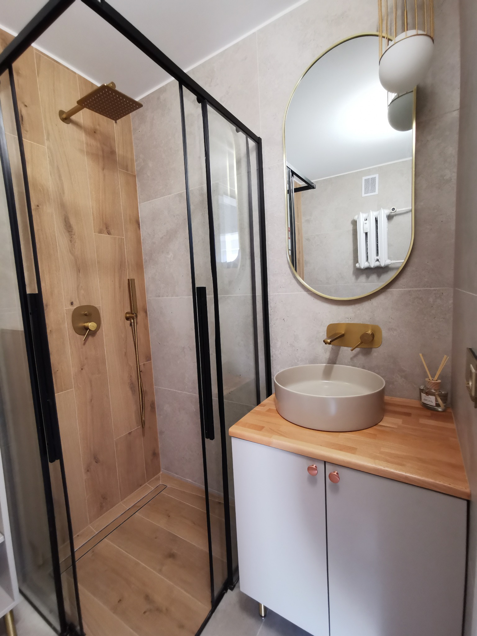 Nowoczesna łazienka z kabiną prysznicową typu walk-in, umywalką nablatową na drewnianym blacie i złotymi akcentami armatury.