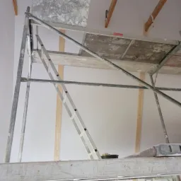 Wnętrze w Krokowej w trakcie prac wykończeniowych; widoczne rusztowanie, ściany przygotowane do malowania lub gładzi, sufit z widocznymi elementami konstrukcyjnymi.