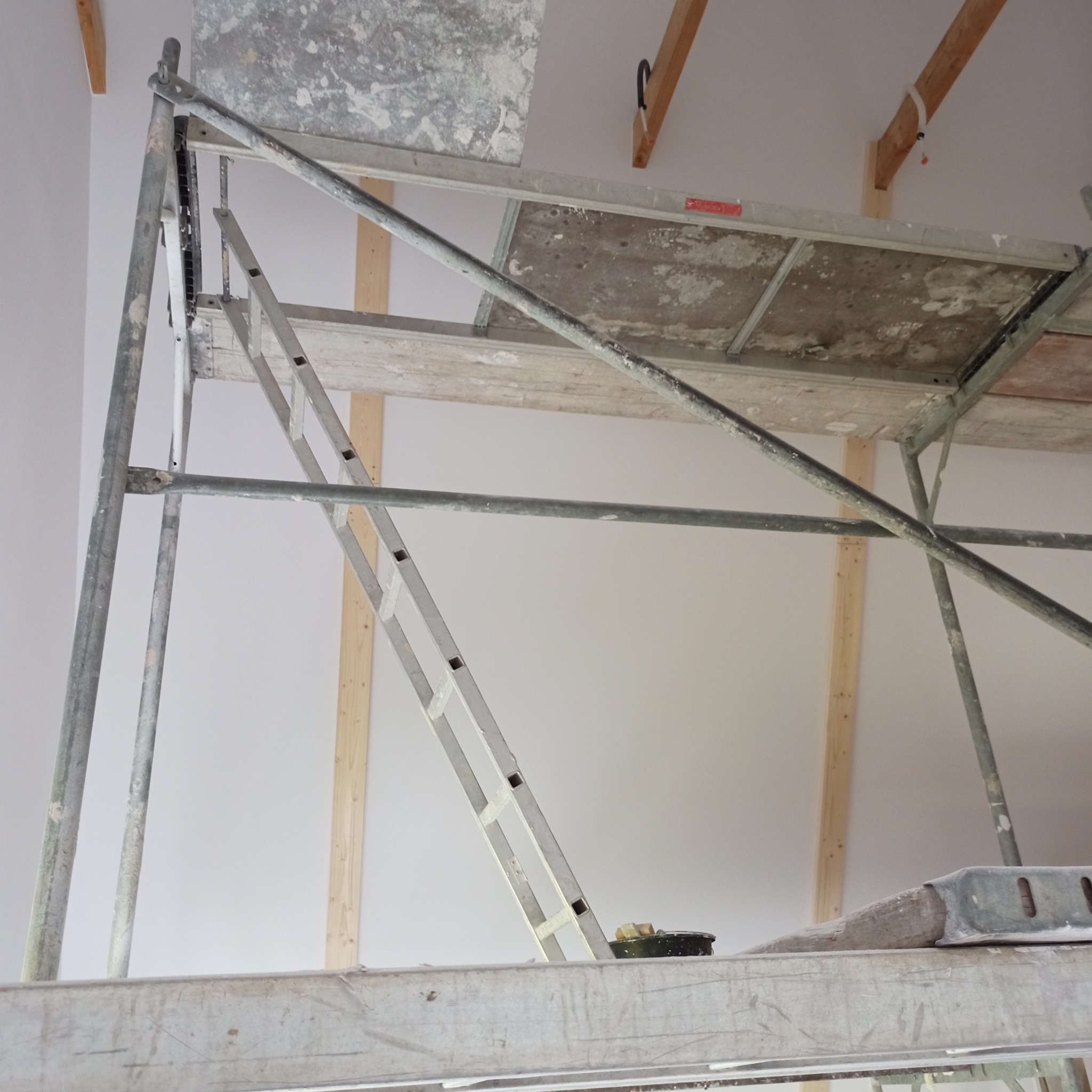 Wnętrze w Krokowej w trakcie prac wykończeniowych; widoczne rusztowanie, ściany przygotowane do malowania lub gładzi, sufit z widocznymi elementami konstrukcyjnymi.