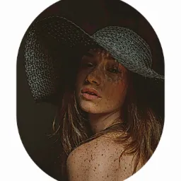 Portret kobiety w kapeluszu z dużym rondem, z piegami na twarzy i ramionach, w ciemnym otoczeniu, wykonany w Poznaniu.