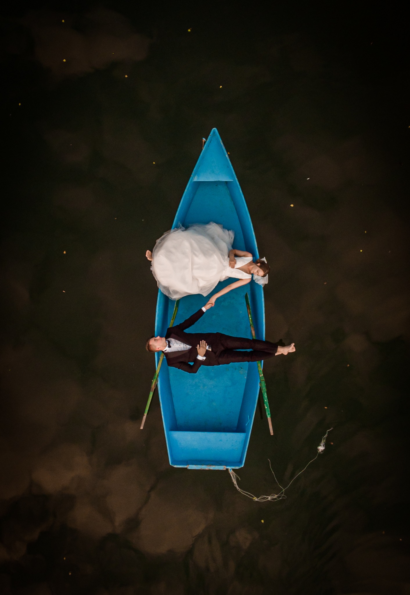 Para młoda w Słubicach leżąca w błękitnej łódce na wodzie, widok z góry, panna młoda w białej sukni, pan młody w brązowym garniturze.