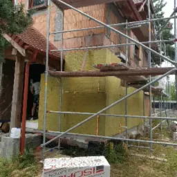 Dom w trakcie ocieplania wełną mineralną, widoczne rusztowania i paczka materiału izolacyjnego ISOROC