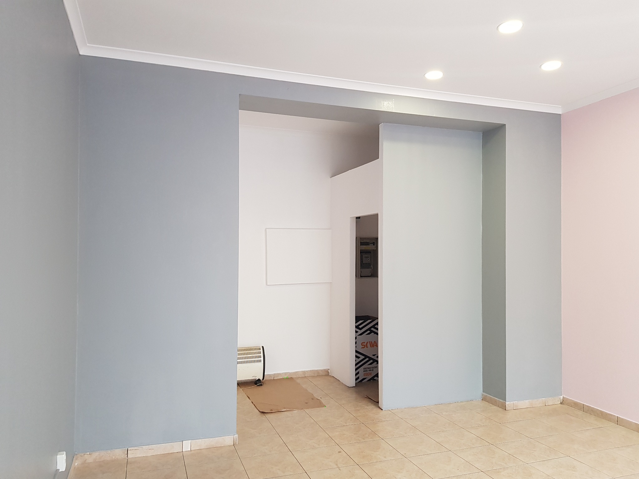 Wnętrze po remoncie z pomalowanymi ścianami na szaro i różowo, z widocznymi detalami wykończeniowymi, takimi jak listwy przypodłogowe i sufitowe, oraz otwartym przejściem do innego pomieszczenia...