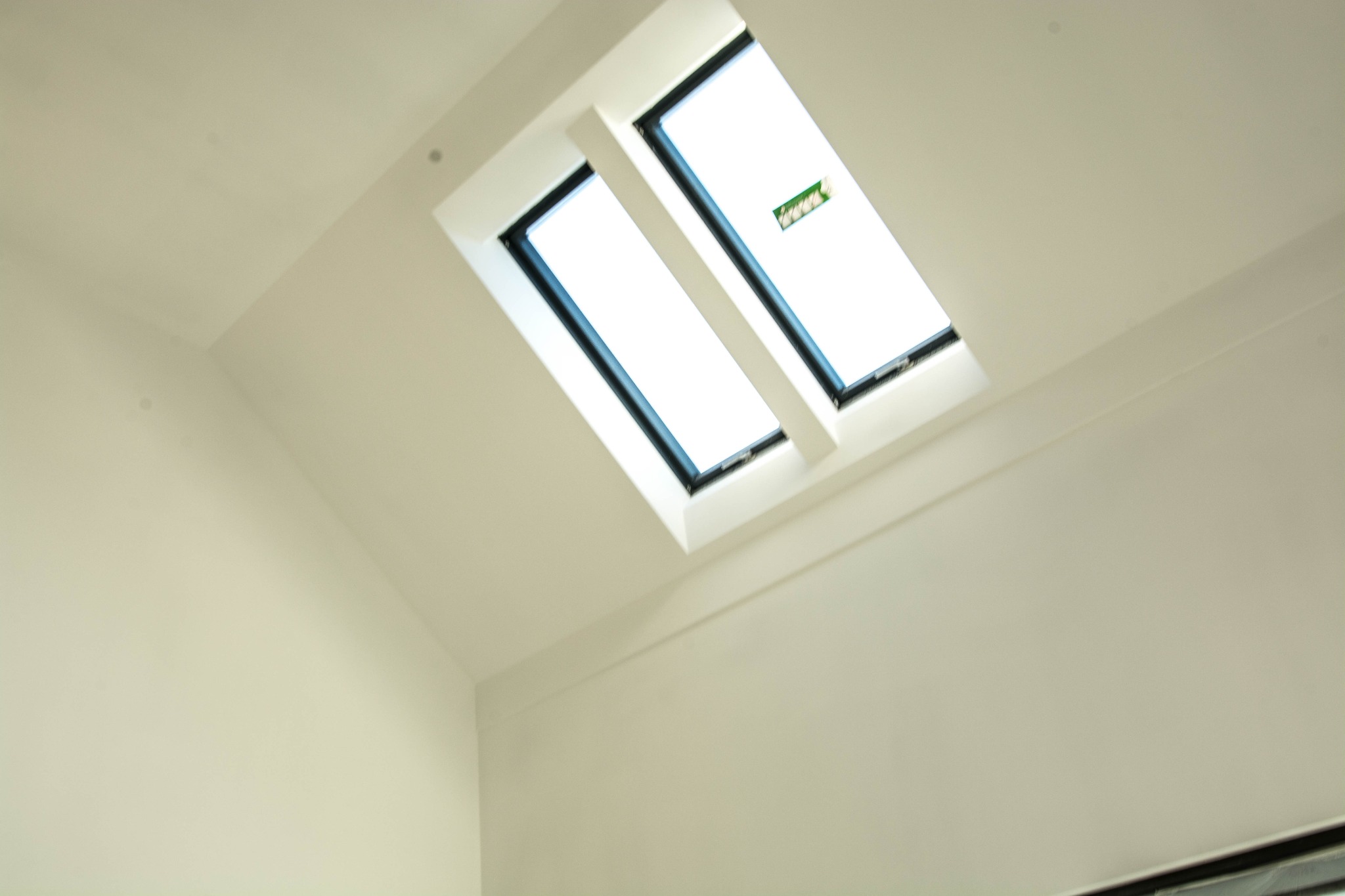 Biały sufit pod skosem z dwoma oknami dachowymi, widoczne delikatne przejścia kolorystyczne i faktura gładzi.