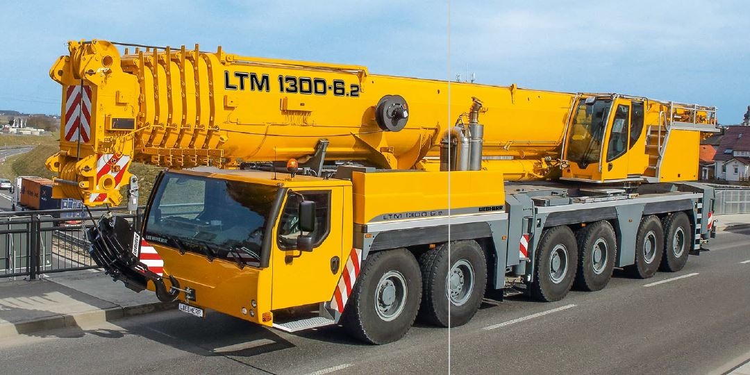 Żółty, teleskopowy dźwig samojezdny Liebherr LTM 1300-6.2 na drodze, widok z boku, z częściowo wysuniętym ramieniem.