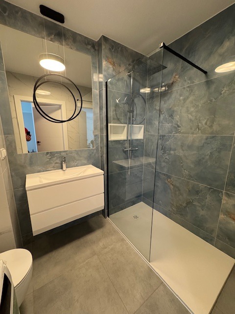 Nowoczesna łazienka z kabiną prysznicową typu walk-in, umywalką nablatową na szafce wiszącej i lustrem z dekoracyjną lampą wiszącą.