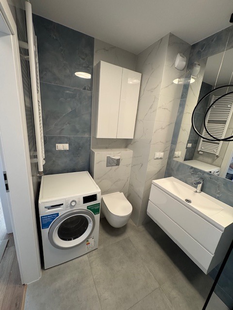 Nowoczesna łazienka w Pruszczu Gdańskim z pralką, umywalką z szafką, toaletą podwieszaną i płytkami imitującymi marmur na ścianach.
