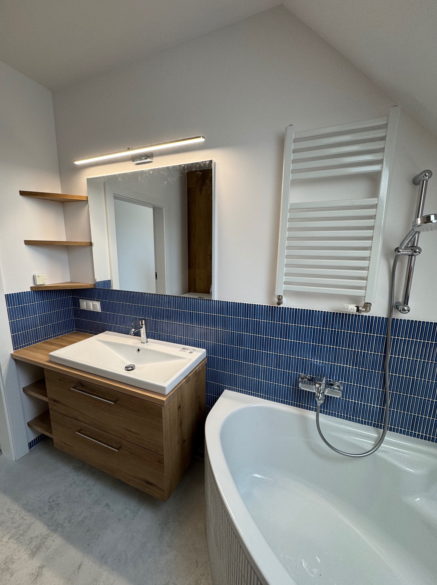 Nowoczesna łazienka z umywalką nablatową na drewnianej szafce, niebieską mozaiką na ścianie i grzejnikiem drabinkowym. Ujęcie z perspektywy.