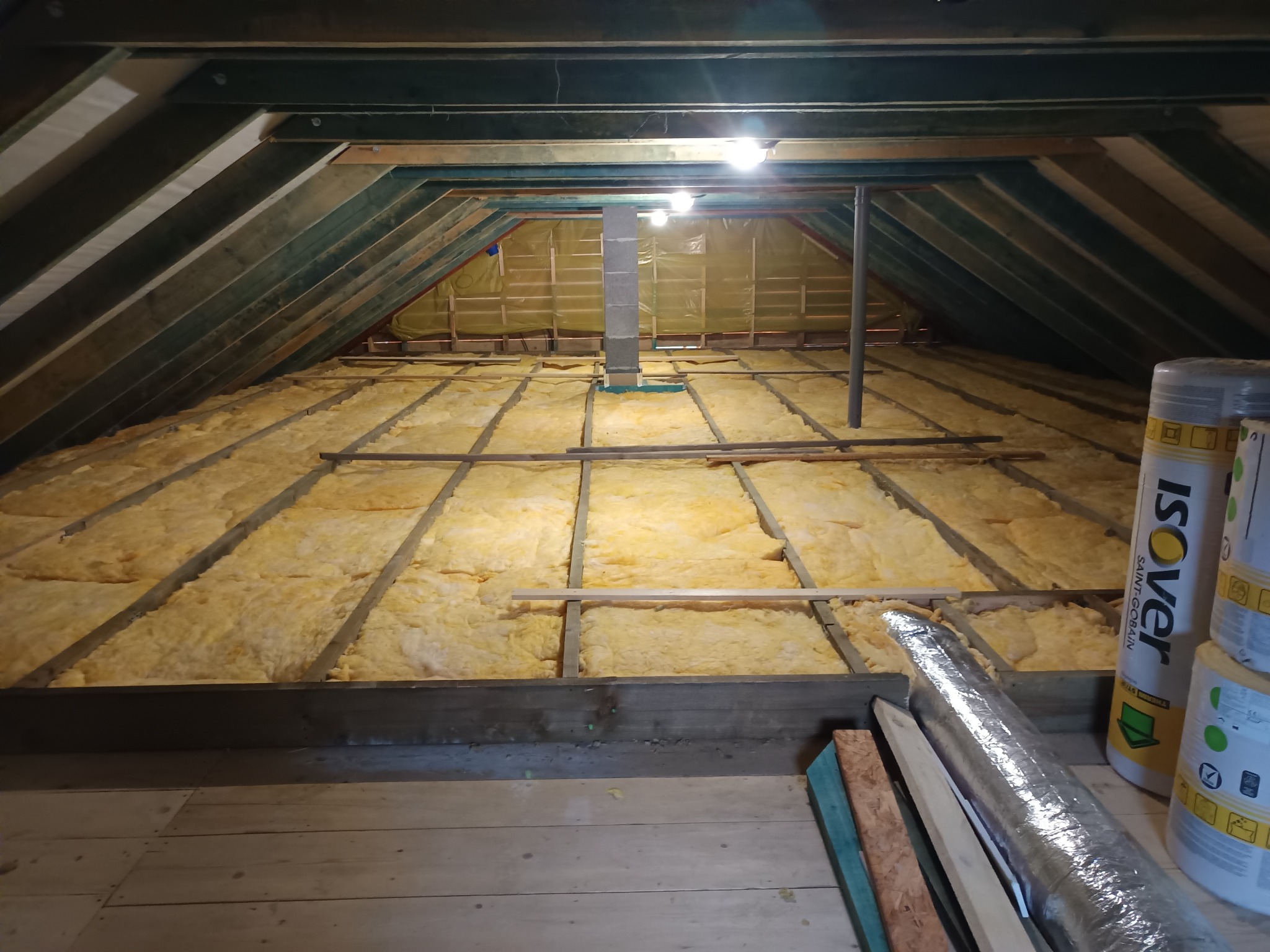 Ocieplenie poddasza wełną mineralną, widoczne belki stropowe, izolacja między nimi, rolka wełny Isover. Prace wykończeniowe na strychu.