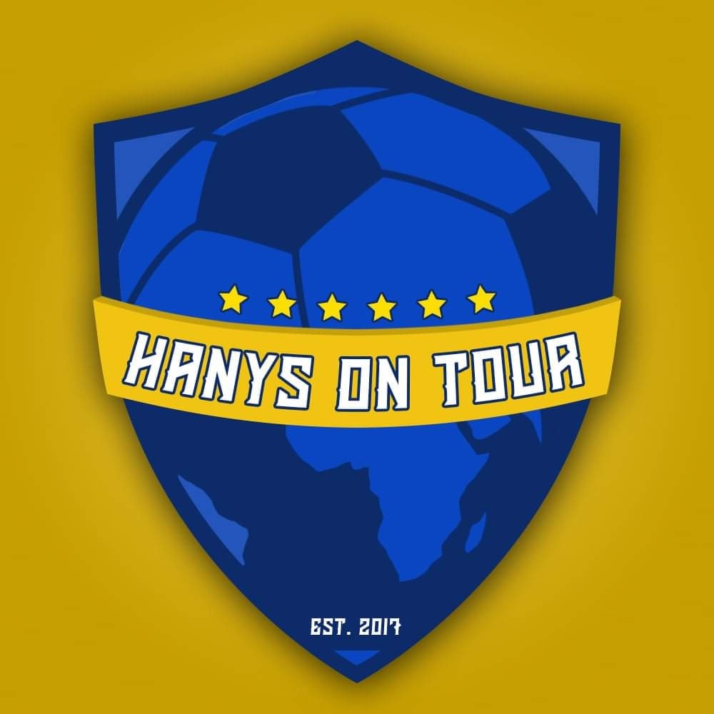 Tarcza z piłką nożną, konturem Afryki, pięcioma gwiazdami i napisem 'HANYS ON TOUR' EST. 2017 na żółtym tle.