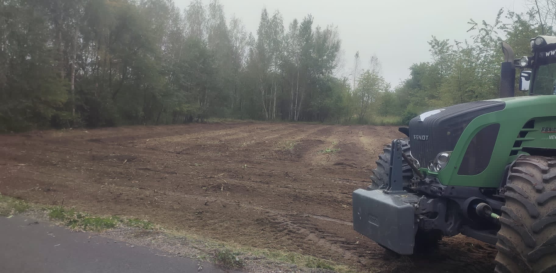 Przygotowane pole po usunięciu drzew, widoczny traktor Fendt z przodu po prawej stronie, w tle las.
