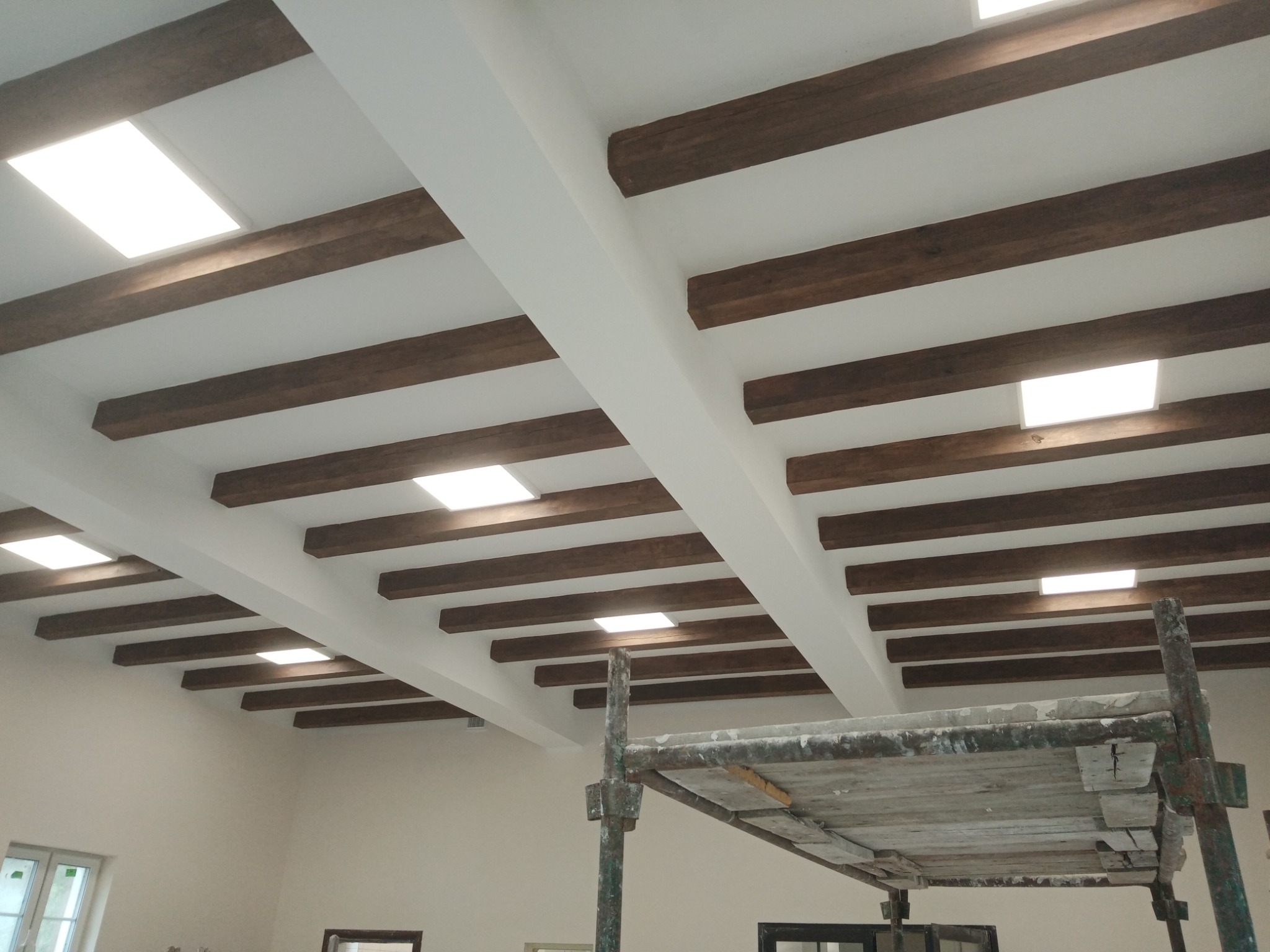 Sufit z drewnianymi belkami i wbudowanym oświetleniem, widoczny fragment rusztowania malarskiego