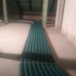 WENT4INSTAL - Zielone rury wentylacyjne rekuperacji ułożone równolegle na poddaszu, widoczne drewniane podpory dachu i fragment ściany z białego pustaka.