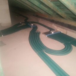 WENT4INSTAL - Zielone, karbowane rury wentylacyjne w izolowanym poddaszu, mocowane do metalowych elementów, widok z góry na instalację.