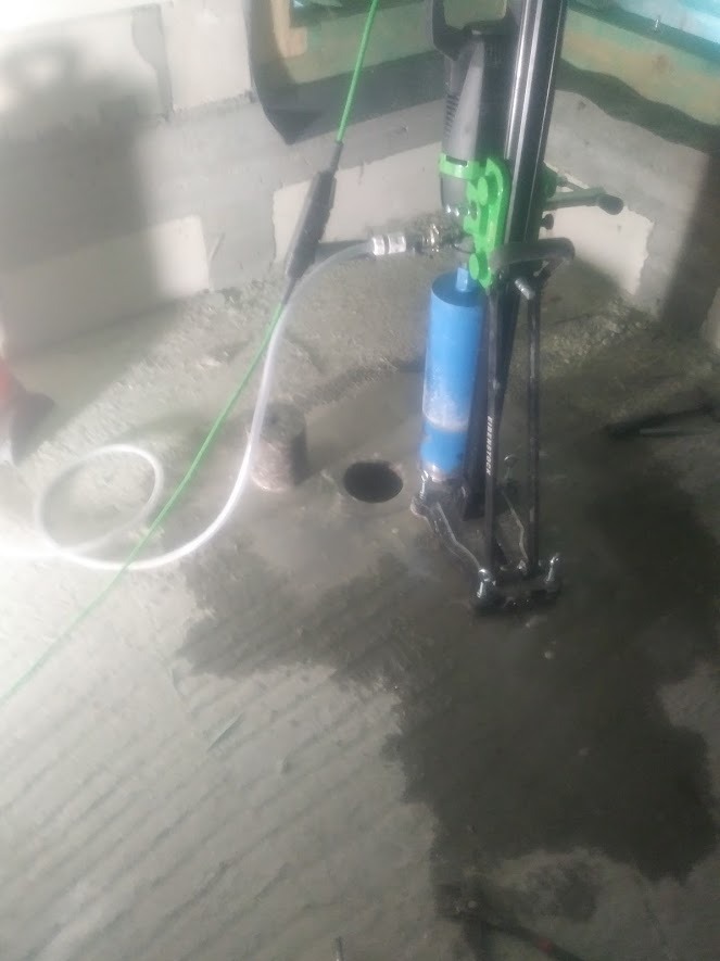Wiercenie rdzeniowe w betonie pod instalację, widoczny wiertło koronowe, woda chłodząca i rdzeń betonowy obok otworu.