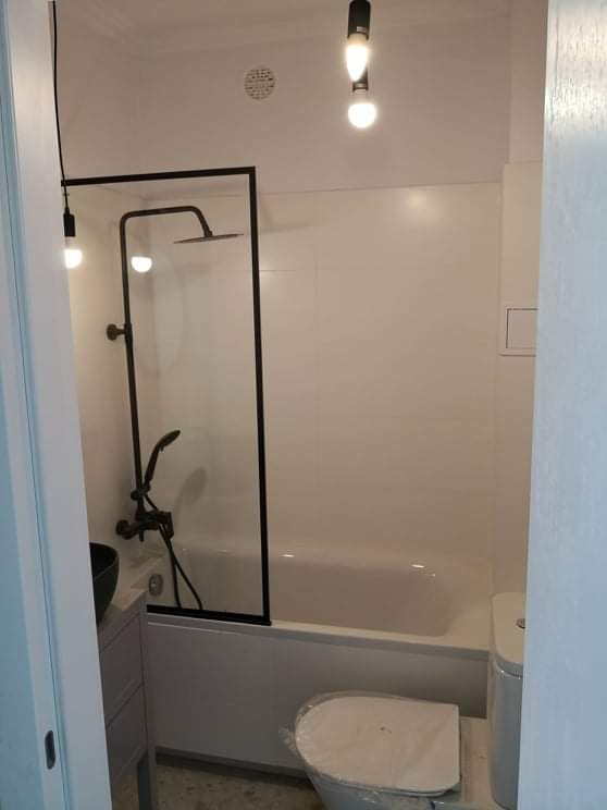 Nowoczesna łazienka w Warszawie z czarną armaturą, kabiną prysznicową i wiszącymi lampami, widok na wannę i toaletę z osłoną.