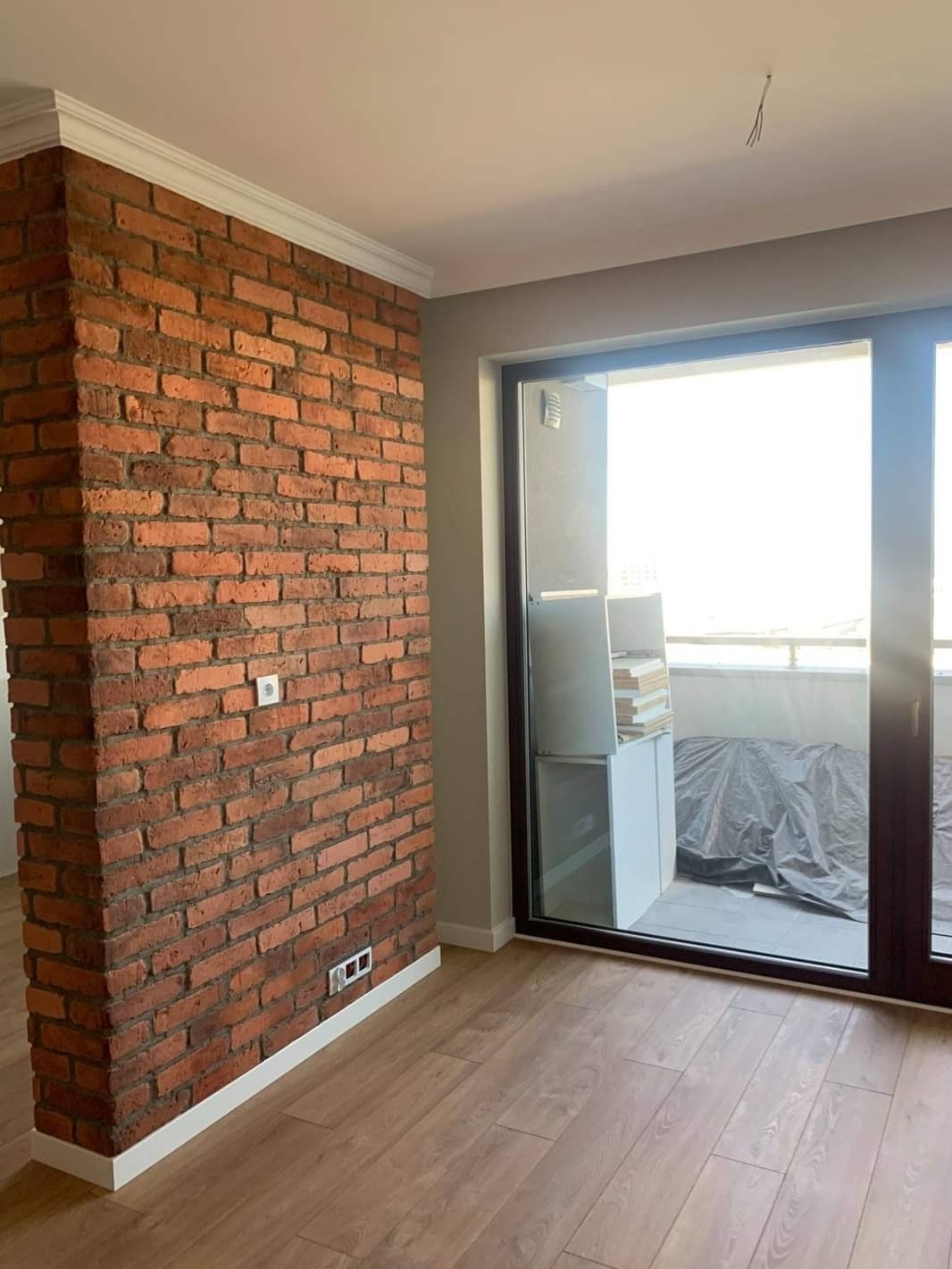 Ceglana ścianka działowa z gładzią i listwami przypodłogowymi w odnowionym mieszkaniu w Warszawie, widok na balkon z przeszkleniem.