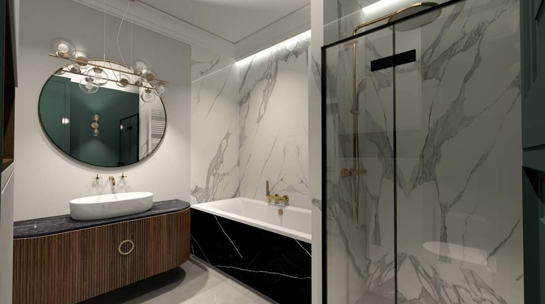 Nowoczesna łazienka z owalną umywalką nablatową, okrągłym lustrem z oświetleniem i kabiną prysznicową ze złotymi detalami na tle marmurowych płytek.