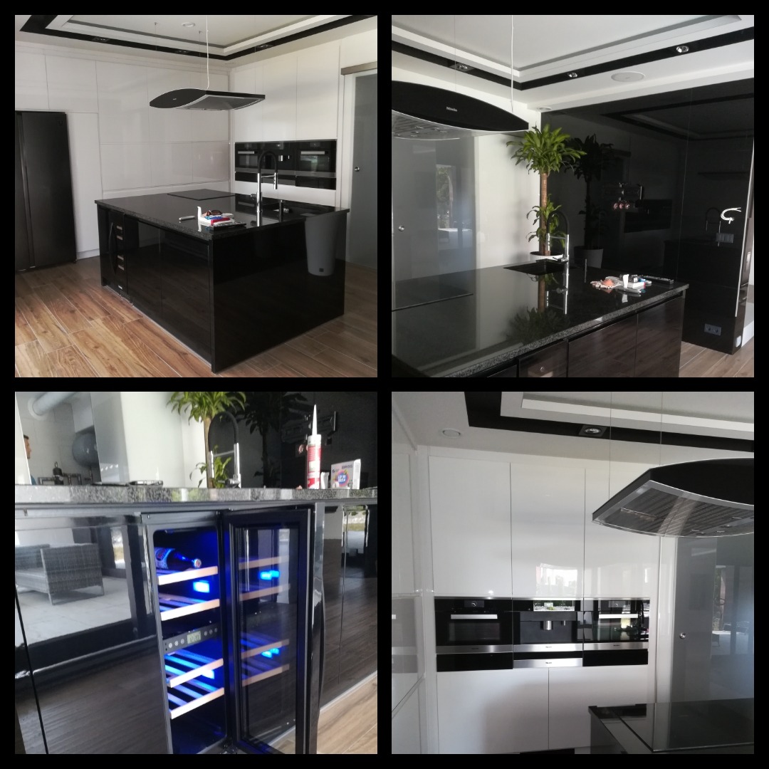 Nowoczesna kuchnia: białe szafki z połyskiem, czarny granitowy blat na wyspie, zabudowane sprzęty AGD i chłodziarka do wina z niebieskim oświetleniem.