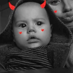 Czarno-białe zdjęcie dziecka z nałożonymi filtrami: czerwone rogi i serduszka na twarzy, w tle osoba z wystawionymi ustami.