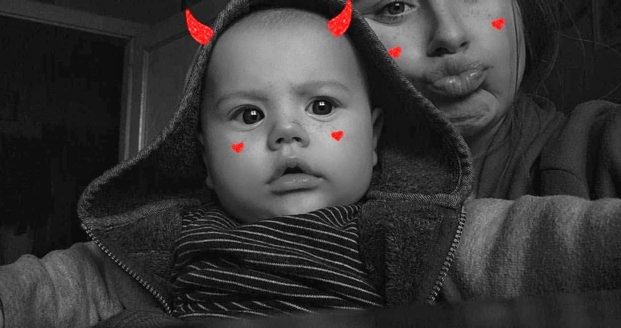 Czarno-białe zdjęcie dziecka z nałożonymi filtrami: czerwone rogi i serduszka na twarzy, w tle osoba z wystawionymi ustami.