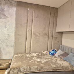 PPHU ADMAR MARTYNA KAŹMIERCZAK - Beżowa sypialnia z tapetą w liście, pluszowym łóżkiem i panelem ściennym. Uwagę zwraca designerska lampka nocna i legowisko dla psa w rogu.