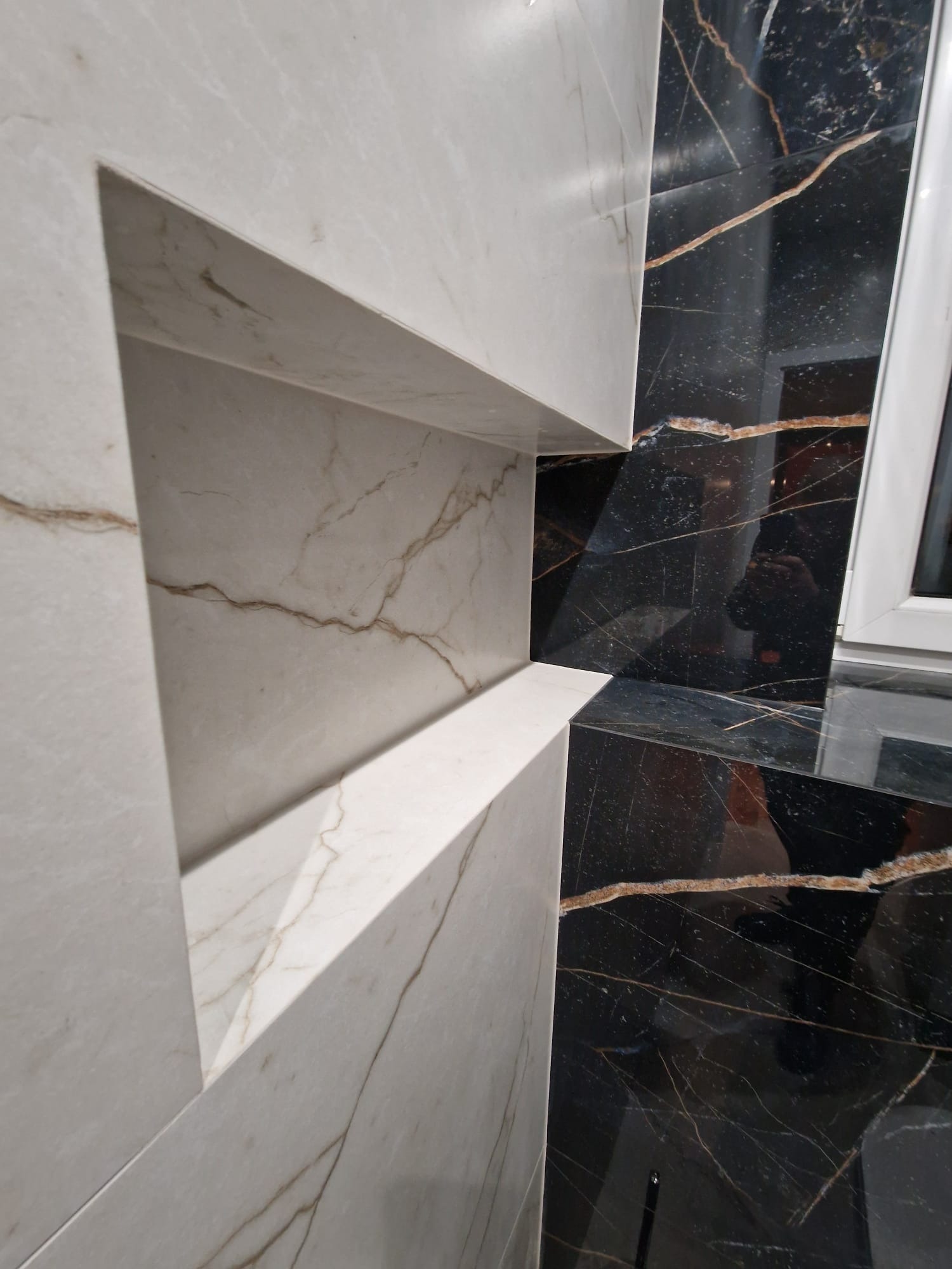 Ściana wykończona płytkami z marmuru w kolorze białym i czarnym z wnęką, widoczna faktura i wzór żyłkowania.