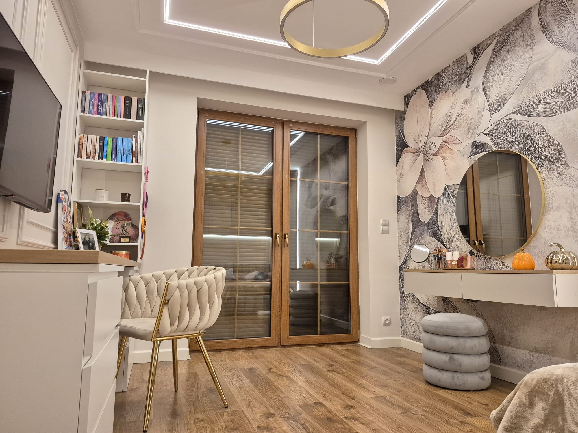 Elegancka sypialnia z toaletką, tapetą w kwiaty i drewnianą podłogą. Krzesło z weluru i złote nogi. Okno z drewnianą ramą i żaluzjami. Nowoczesne oświetlenie sufitowe.