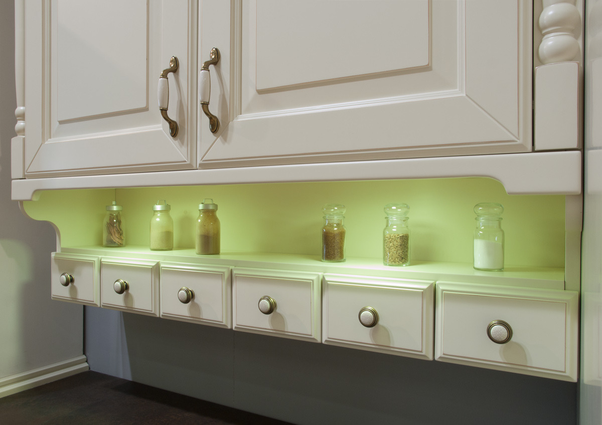 Klasyczne kremowe szafki kuchenne z uchwytami w stylu retro, podświetlana półka z rzędem szuflad i szklanymi pojemnikami z przyprawami.