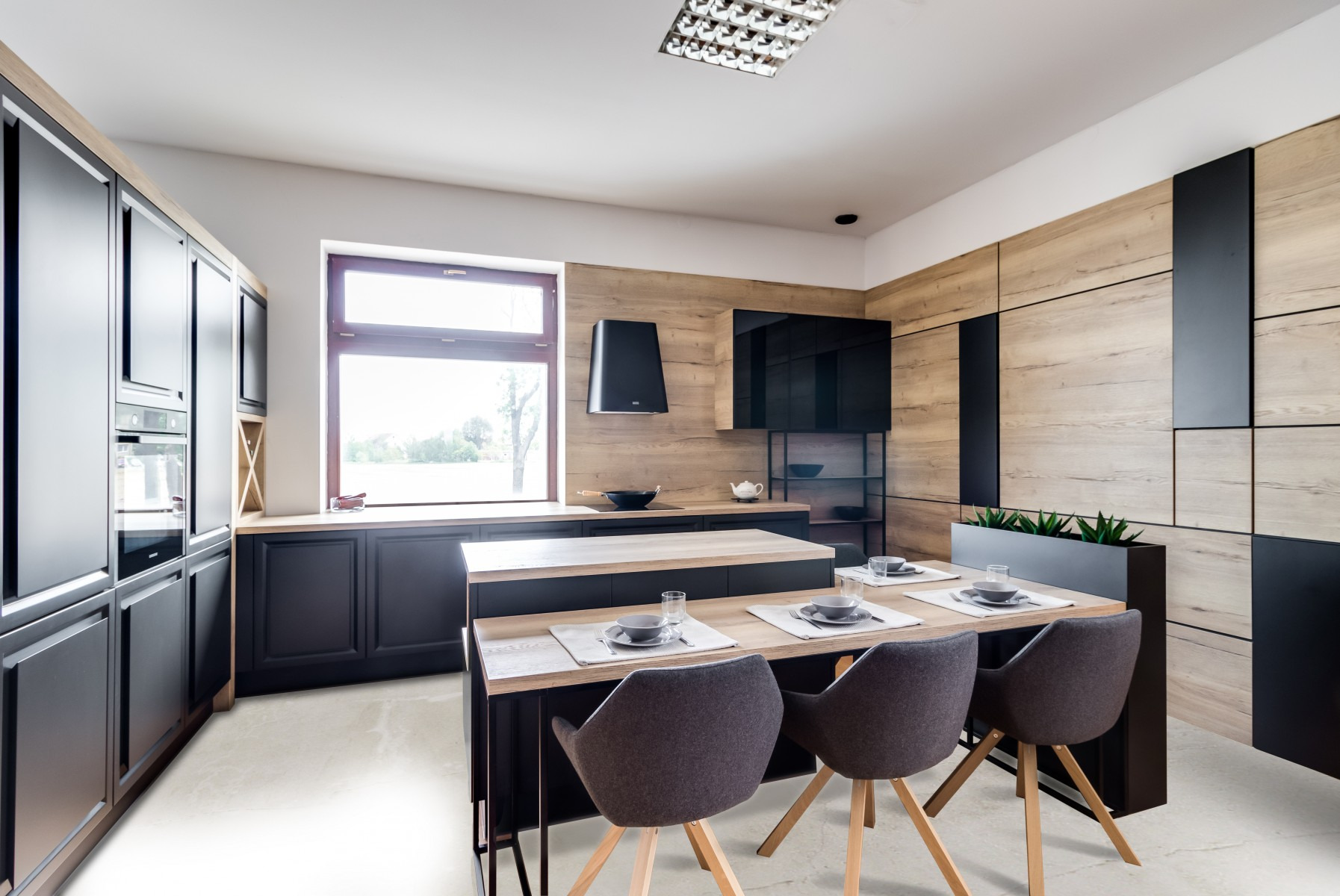 Nowoczesna kuchnia z wyspą i miejscem do jedzenia, czarne szafki z drewnianymi akcentami, drewniana ściana, czarny okap, stół nakryty dla czterech osób, szare krzesła na drewnianych nogach.