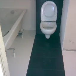 Biała wanna i toaleta na tle kontrastujących, czarnych płytek podłogowych i ściennych w łazience po remoncie.