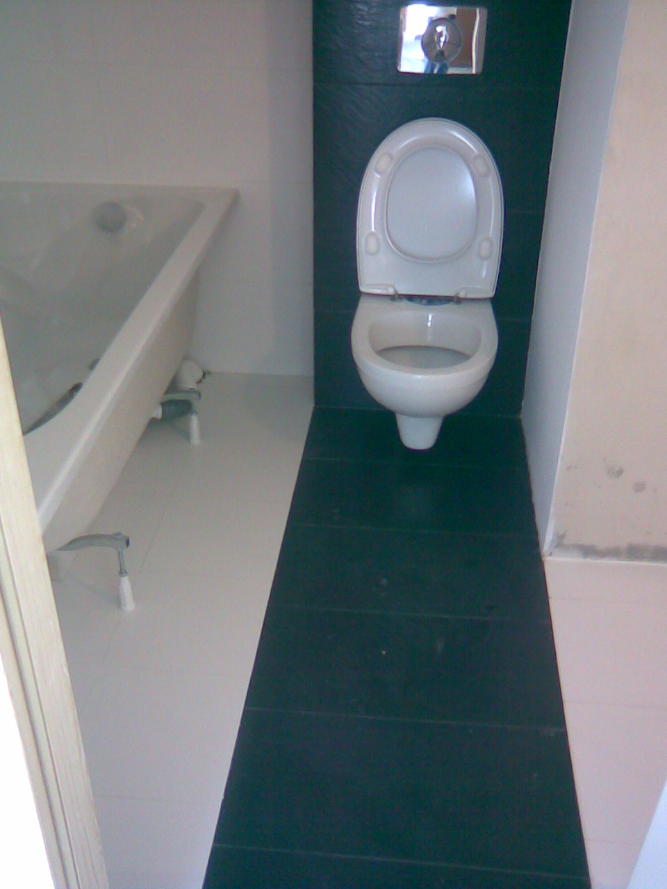 Biała wanna i toaleta na tle kontrastujących, czarnych płytek podłogowych i ściennych w łazience po remoncie.