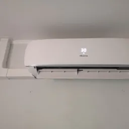 Biała klimatyzacja Hisense zamontowana na ścianie, wyświetlacz pokazuje temperaturę 30 stopni Celsjusza, widoczne przewody w białej obudowie.