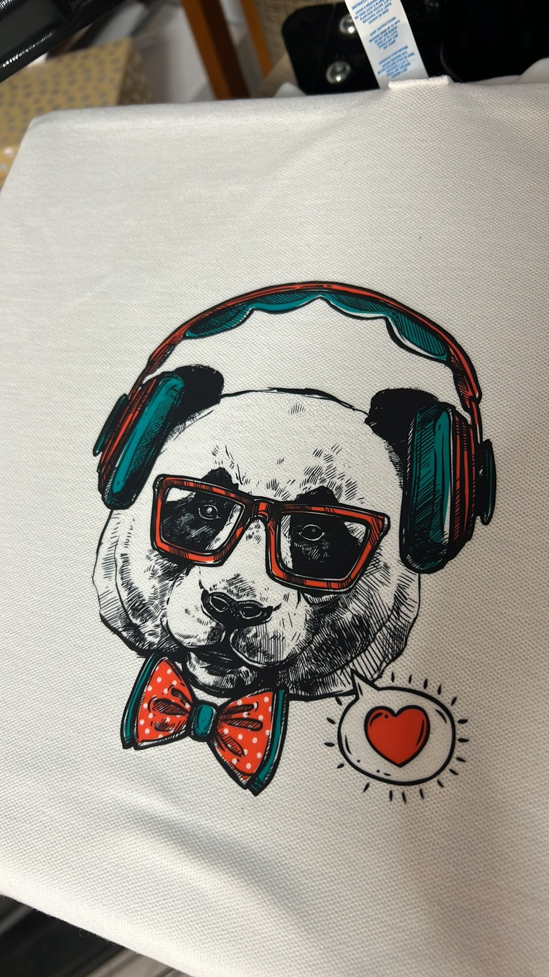 Biała koszulka z nadrukiem pandy w słuchawkach, okularach i muszce z motywem serca w dymku.