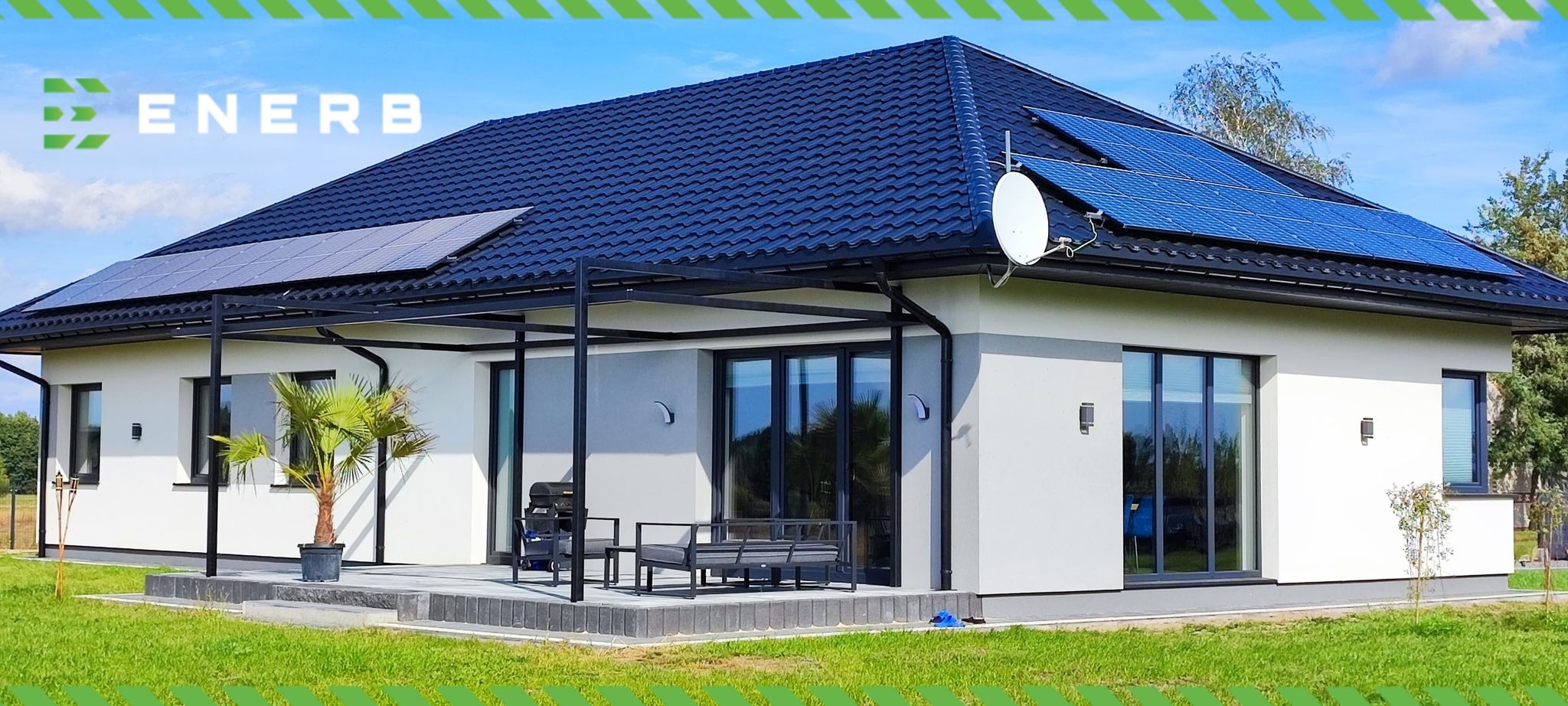 Nowoczesny dom jednorodzinny z ciemną dachówką i panelami słonecznymi na dachu, antena satelitarna, taras z meblami ogrodowymi i palmą w donicy, trawnik.