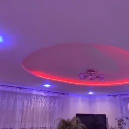 Okrągły sufit podwieszany z czerwonym oświetleniem LED, kryształowy żyrandol, zasłony z koronkowym wzorem i telewizor w salonie z fioletowym oświetleniem.