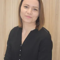 Uśmiechnięta kobieta w czarnej bluzce z guzikami na tle drewnianej ściany, portret.