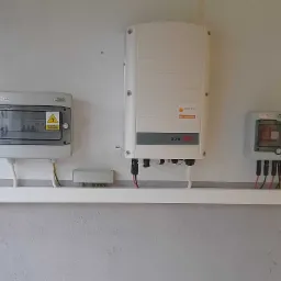 Zamontowany inwerter SolarEdge z dwoma skrzynkami zabezpieczeń na ścianie, widoczne przewody i rurki instalacyjne.