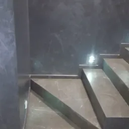 Schody wykończone szarym gresem, ściana pokryta dekoracyjną szarą farbą ze smugami, małe oświetlenie LED na ścianie przy schodach.