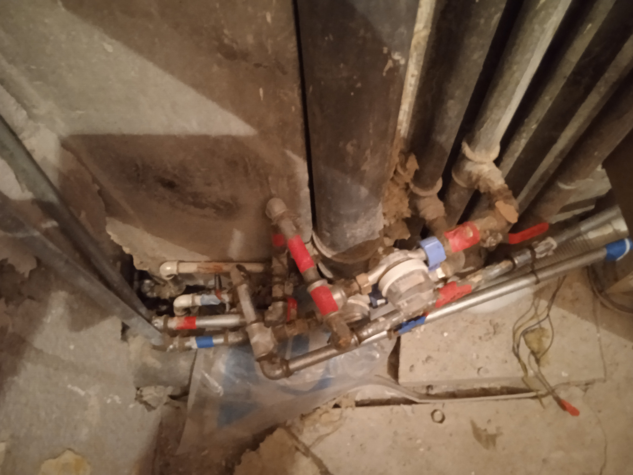 Złożony system rur z zaworami z czerwonymi i niebieskimi uchwytami, instalacja wodna w trakcie prac w surowym wnętrzu z widocznymi przewodami i elementami konstrukcyjnymi.