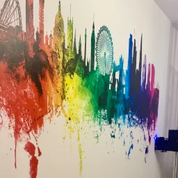 Wielobarwna panorama Londynu nanoszona na ścianę za pomocą specjalistycznej drukarki pionowej, z widoczną głowicą drukującą i konstrukcją urządzenia.