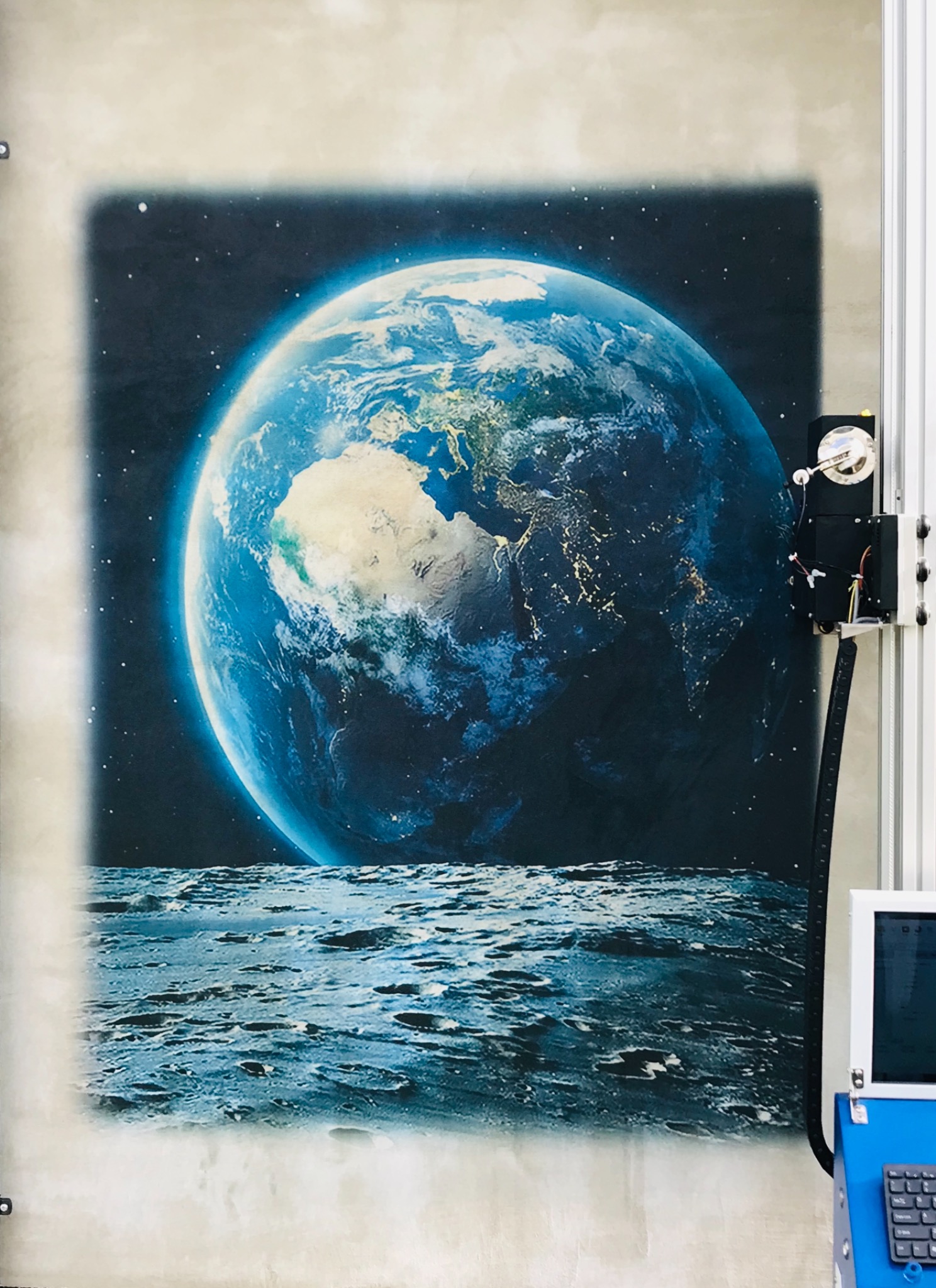 Automatyczny ploter pionowy drukuje obraz Ziemi widzianej z Księżyca na ścianie.