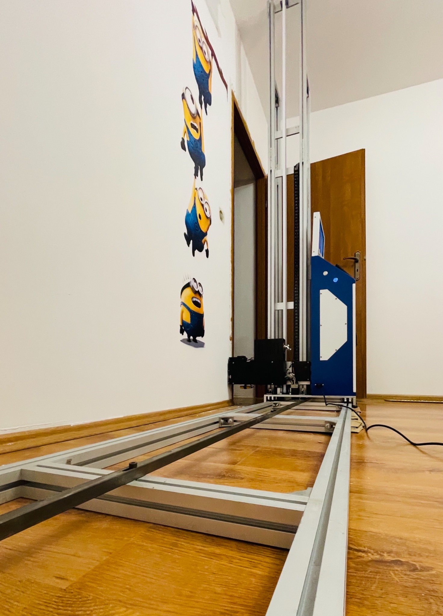 Maszyna do druku pionowego na ścianie, z nadrukowanymi postaciami Minionków na ścianie w tle.