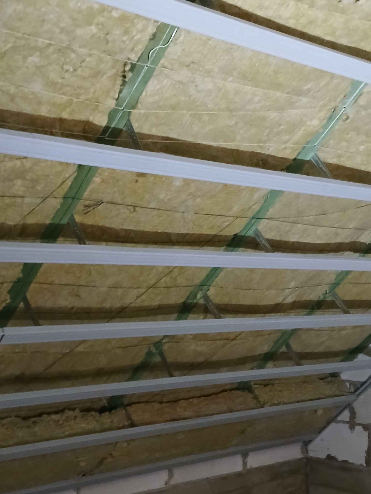 Izolacja poddasza wełną mineralną, widoczne metalowe profile konstrukcyjne i fragment ściany z bloczków.