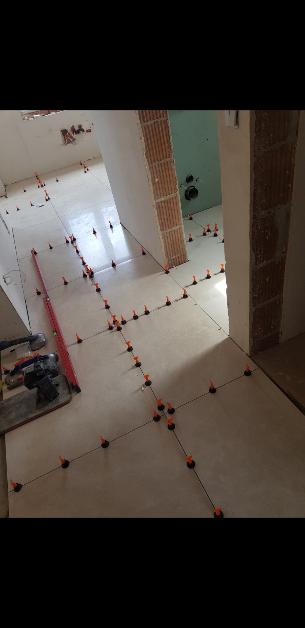 Układanie płytek podłogowych z użyciem systemu poziomowania, widoczne narzędzia glazurnicze i poziomica